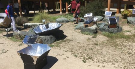 High school students at Sacramento School of Engineering and Sciences demonstrating student-built solar cookers during a solar cooking project